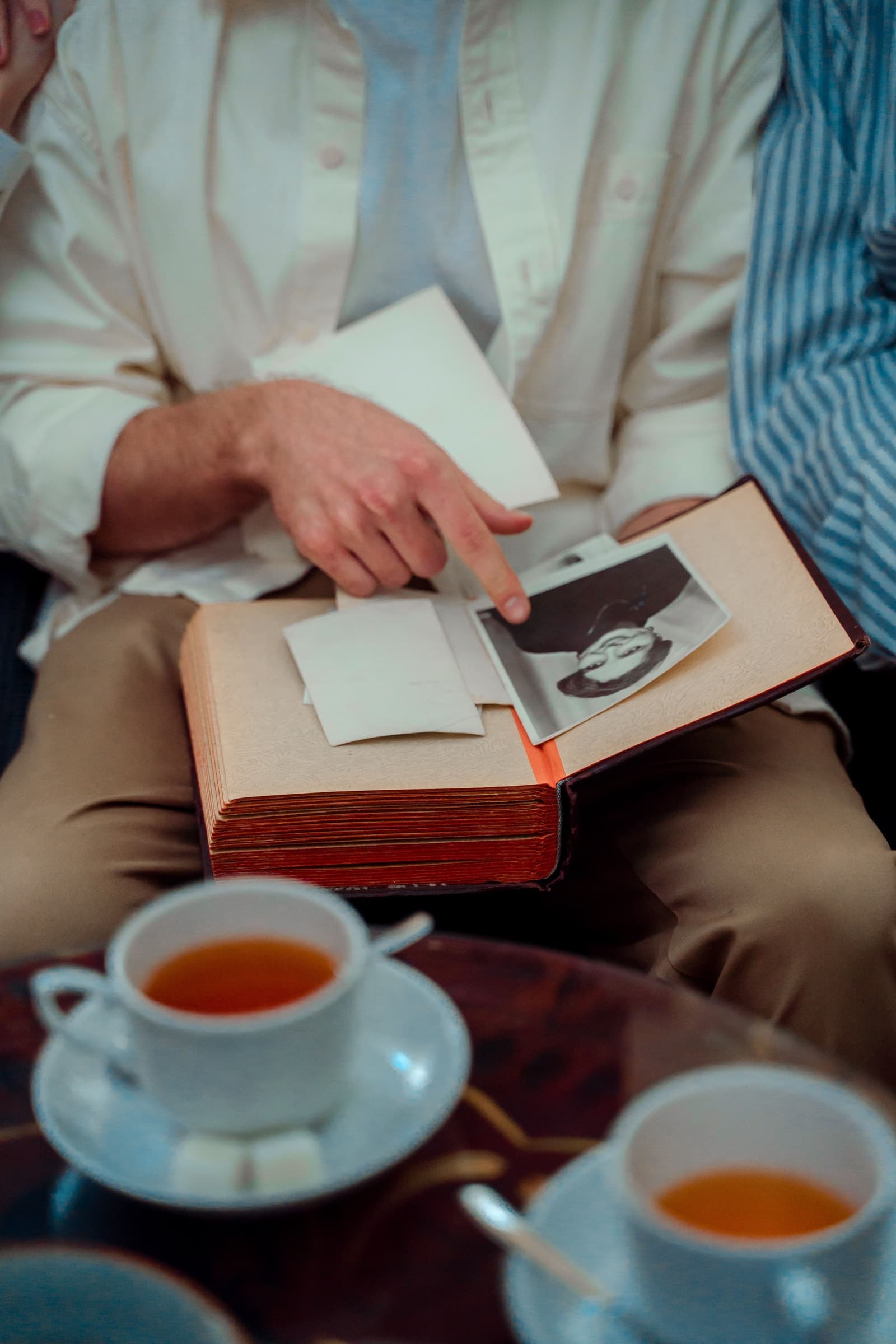 Hands turning the pages of an old family photo album beside a cup of tea