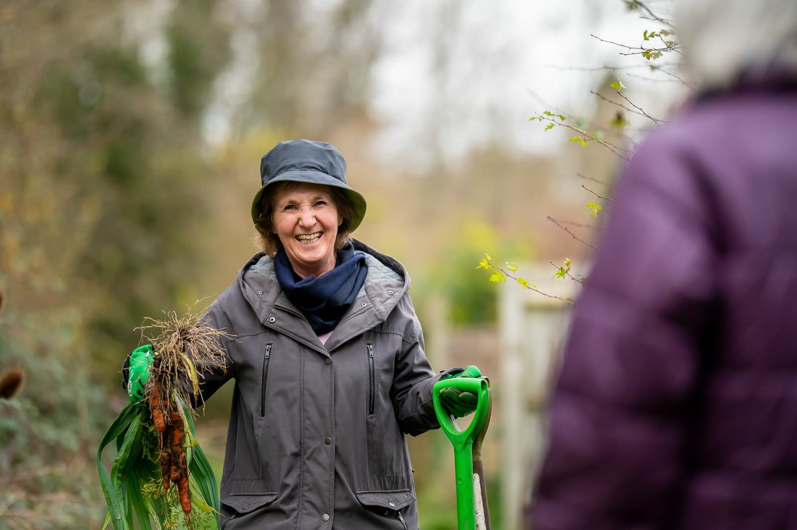 A woman in her seventies grinning in her garden, spade in hand